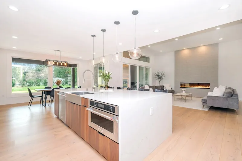 Open-plan kitchen with a white waterfall island and walnut base cabinets, opening onto a living room