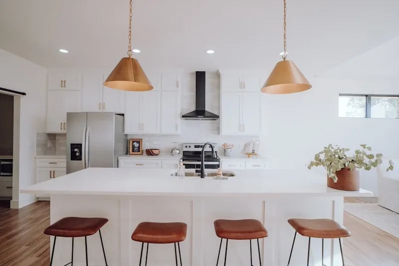 White Shaker kitchen island with a sink, brass pendant lights, and four leather counter stools
